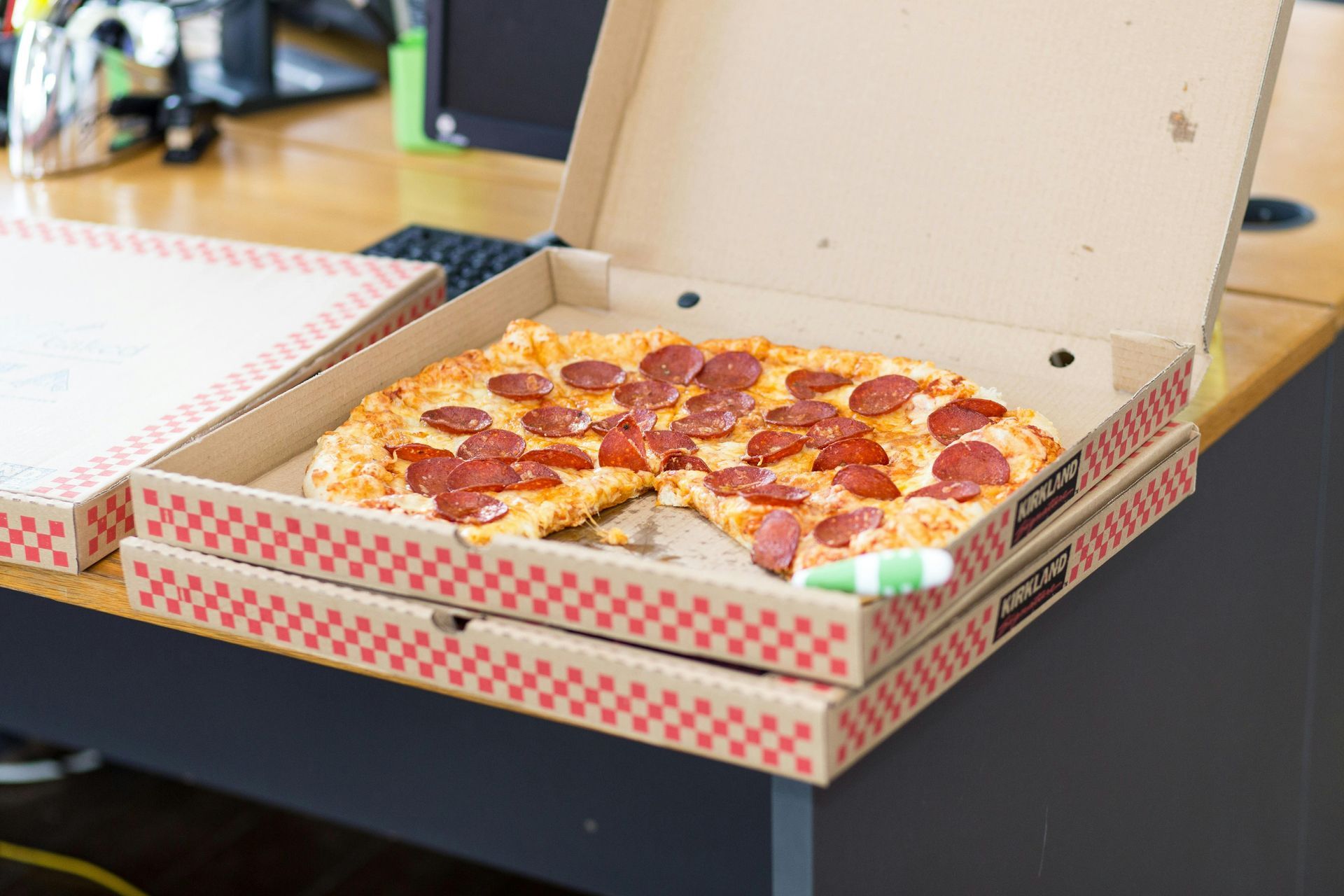 Pizza de pepperoni en cajas abiertas sobre un escritorio, a la que le falta una porción.