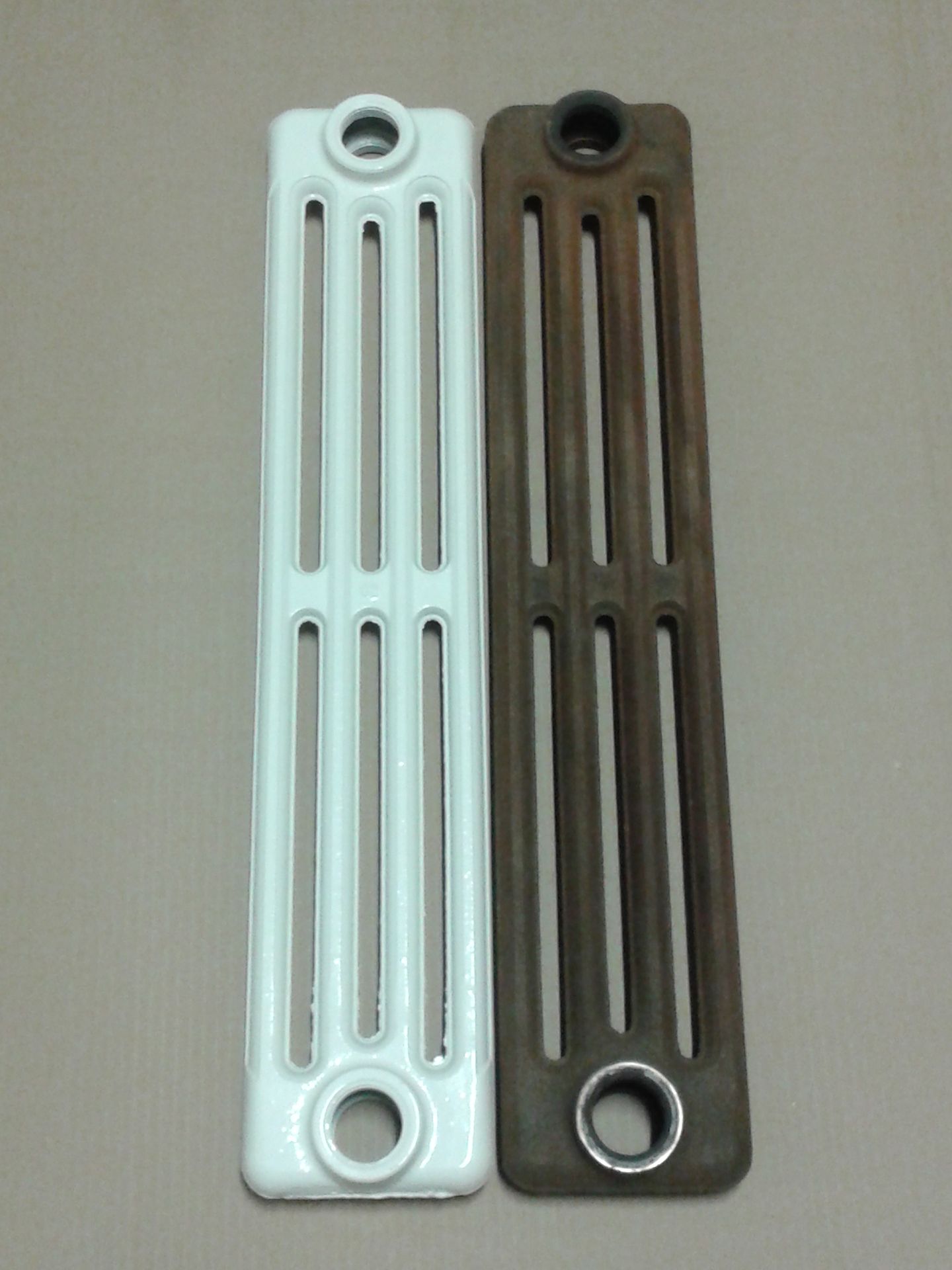 Deux grilles de radiateur, celle à gauche étant blanche et thermolaquée, l'autre sombre à gauche décapée