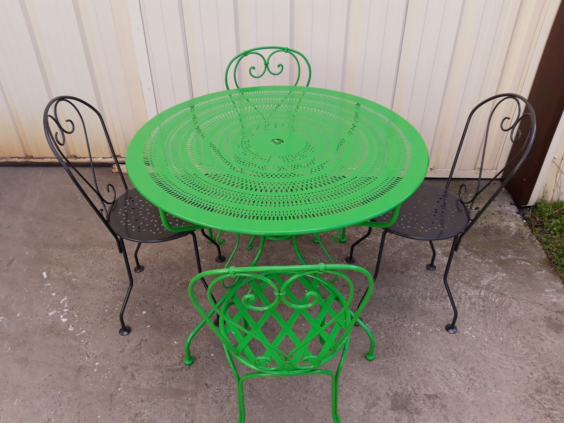Table de jardin verte avec quatre chaises, dont deux pas encore décapées
