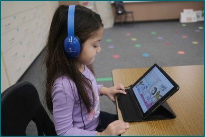 A little girl wearing headphones is using a tablet computer.