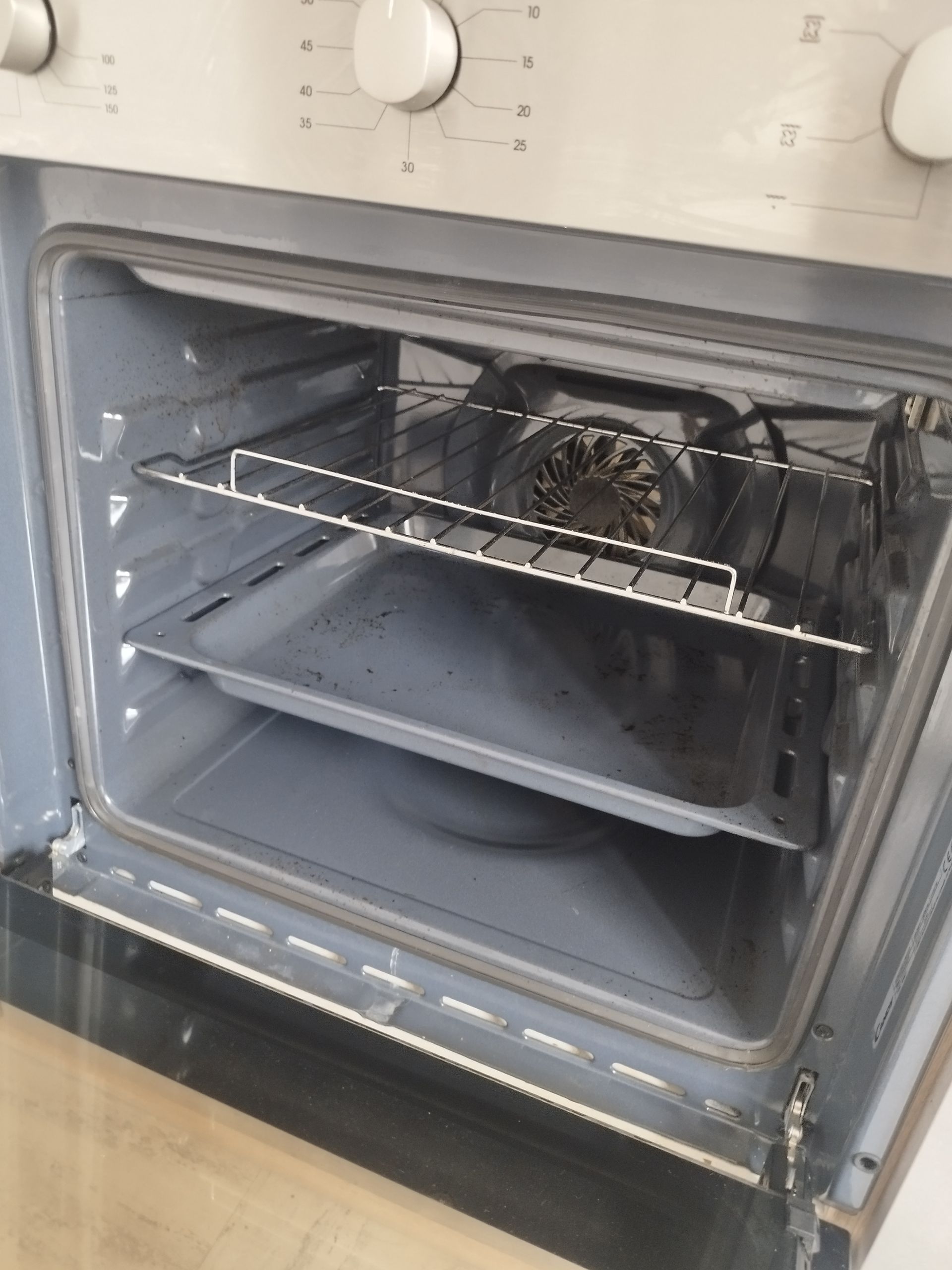 Un four gris clair, porte ouverte, laissant apparaître une grille et une plaque de cuisson à l'intérieur.