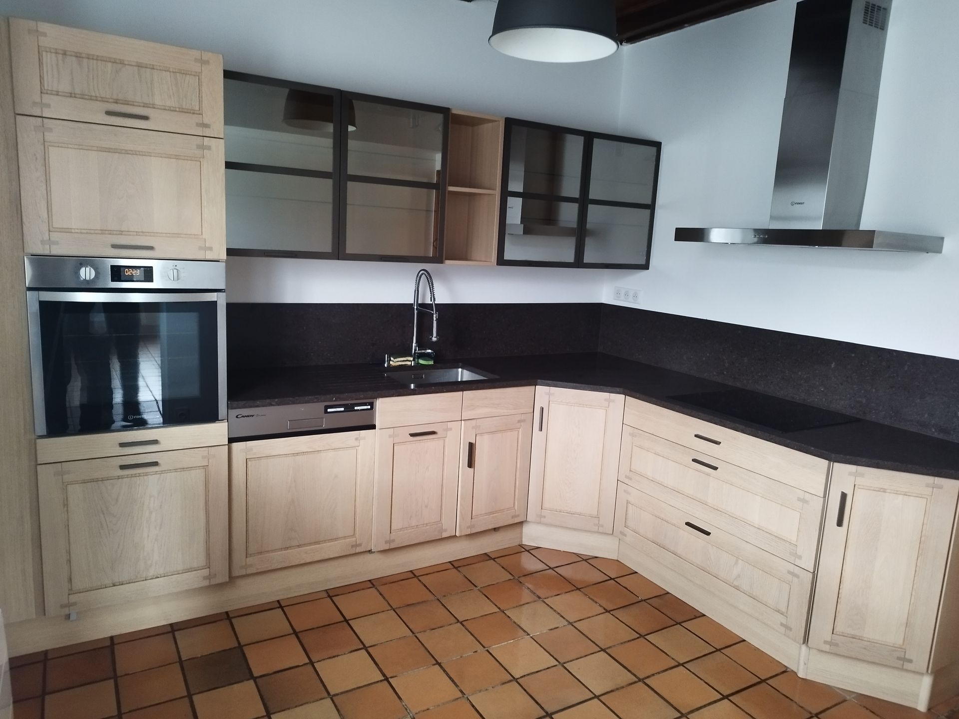 Cuisine moderne avec placards en bois clair, plans de travail foncés, four encastré, hotte aspirante en inox et sol carrelé.