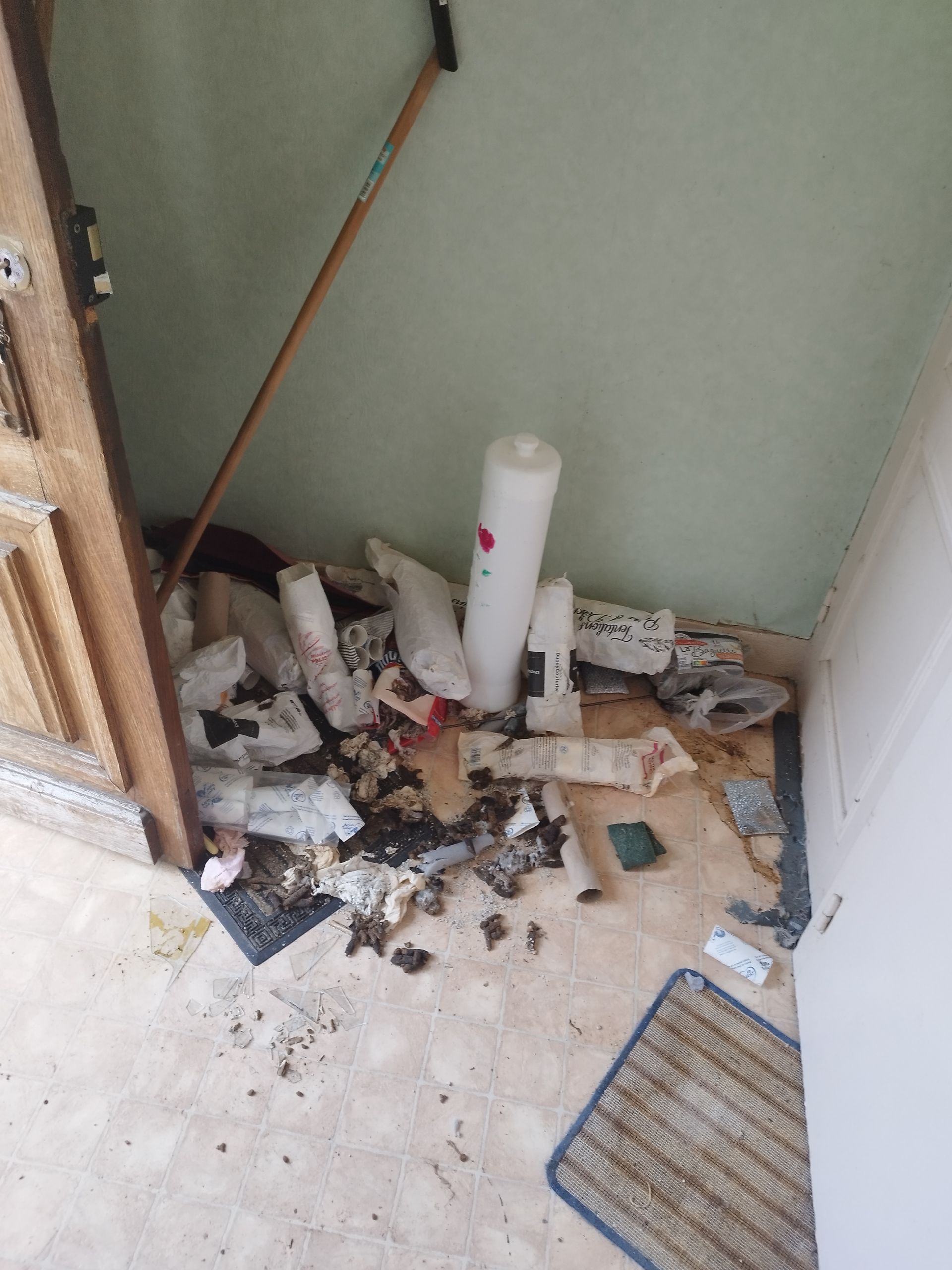 Un tas d'ordures, de débris et un objet cylindrique blanc se trouvent dans un coin d'une pièce.