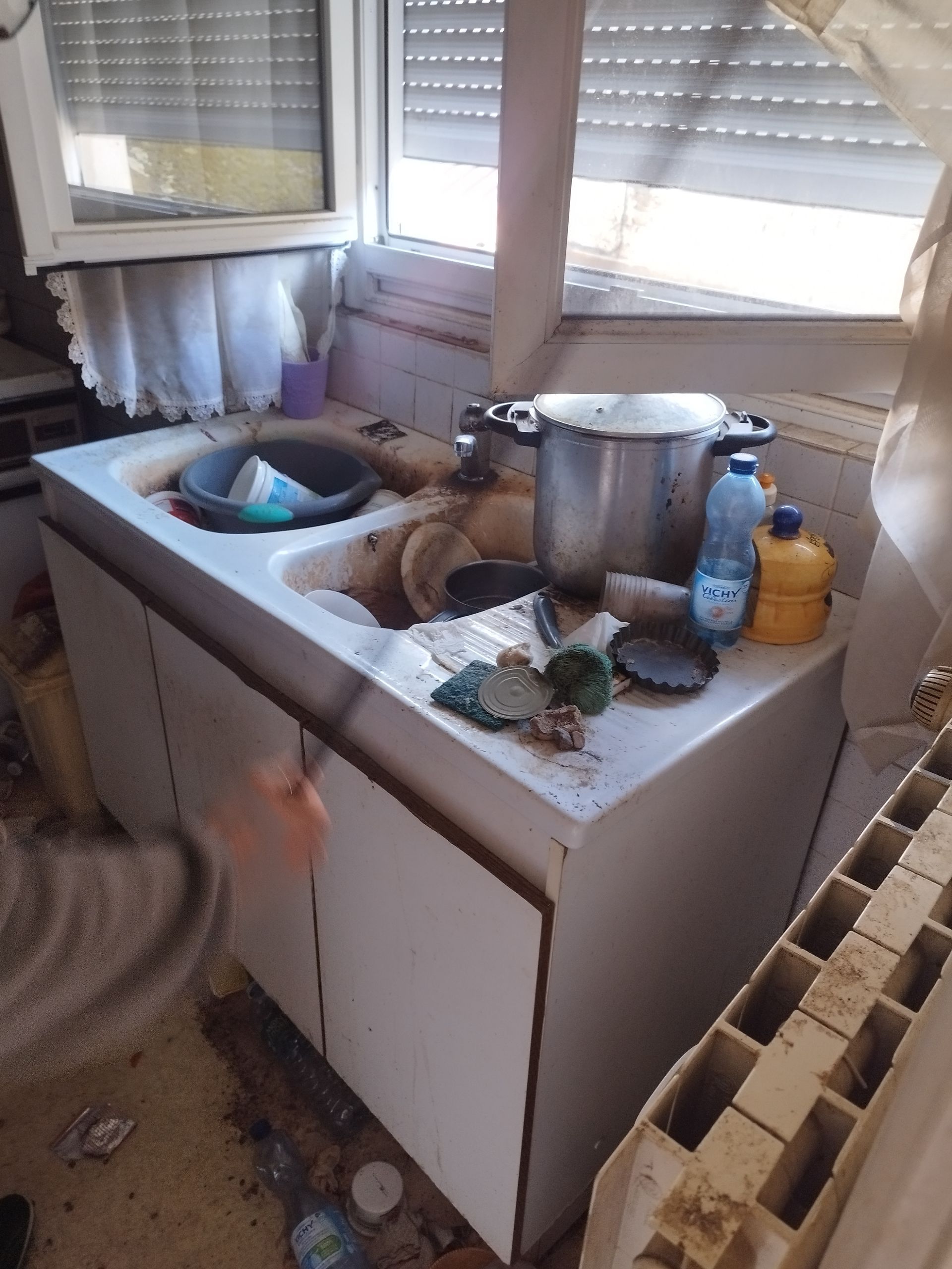 Un évier de cuisine encombré de vaisselle sale, d'une grande casserole et d'une bouteille en plastique.