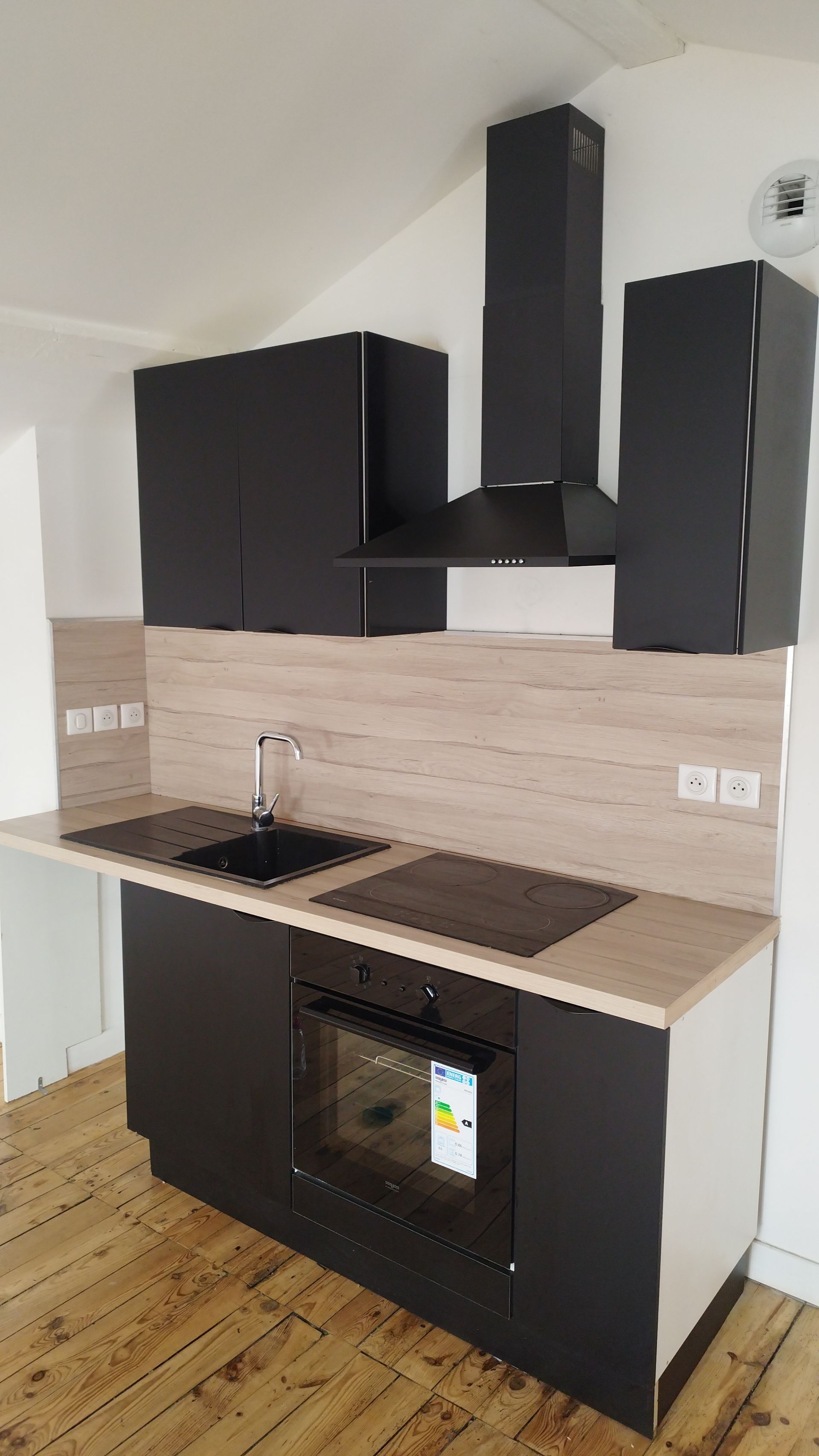Un meuble de cuisine moderne avec des armoires foncées, un plan de travail en bois clair, un évier noir, un four encastré et une hotte aspirante.