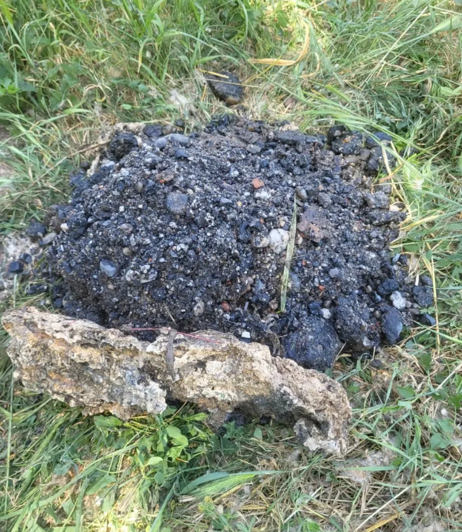 Un montón oscuro y carbonizado de tierra o ceniza sobre la hierba, junto a una roca de color claro.