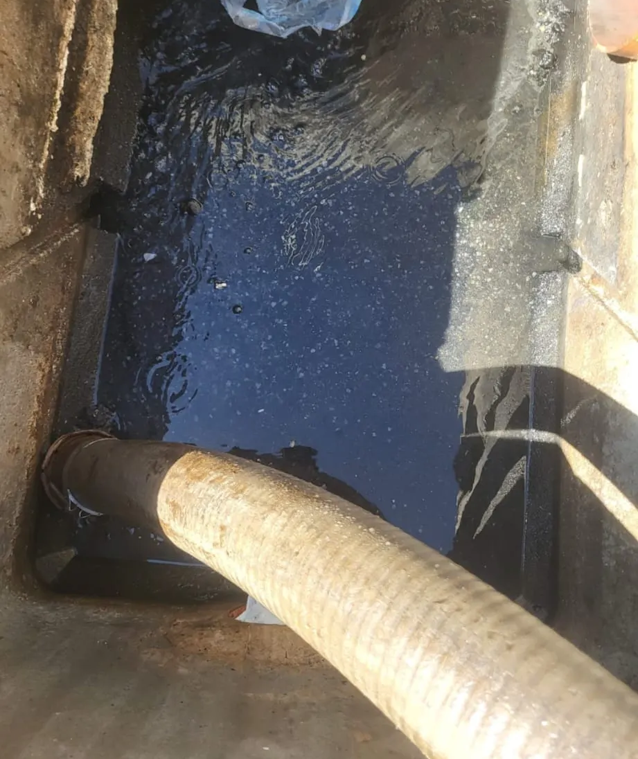 Agua sucia en un pozo estrecho con una manguera que desagua en él.