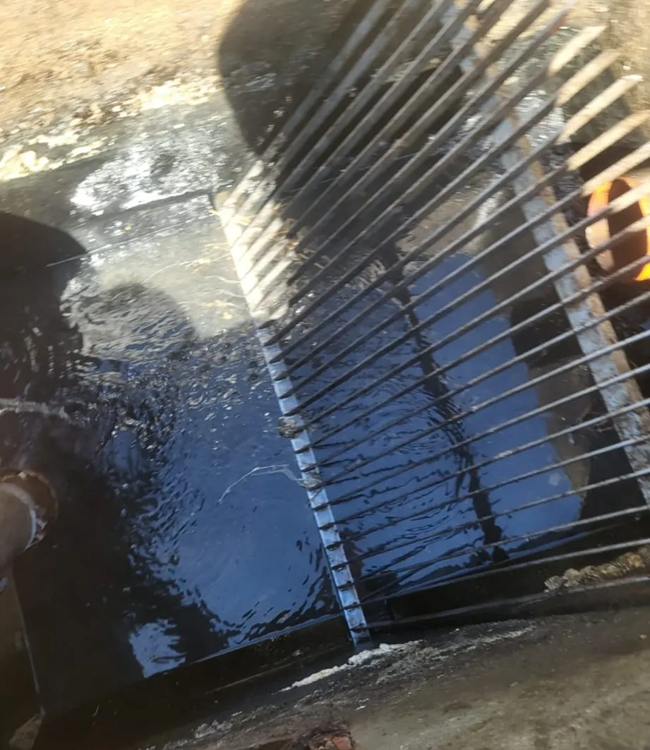 Agua que corre sobre una rejilla metálica en un canal de drenaje, con reflejos azules.