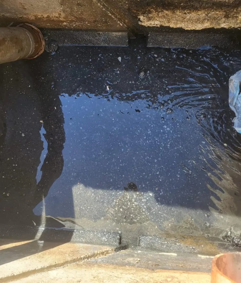 Agua oscura y poco profunda en una poza de hormigón, con un pequeño reflejo del cielo.