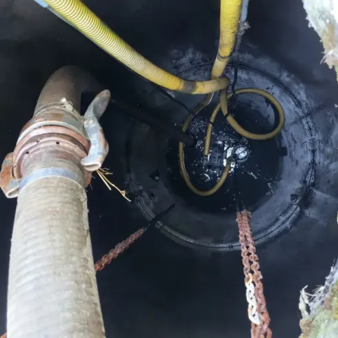 Dentro de un oscuro pozo de servicio, unas mangueras y tuberías se adentran en el agua estancada.