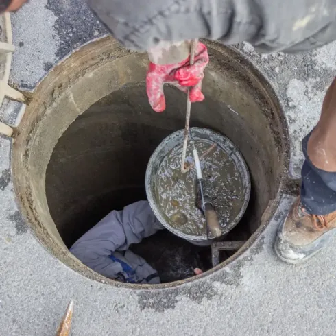 Un trabajador bajando un cubo redondo por una alcantarilla durante tareas de mantenimiento subterráneo