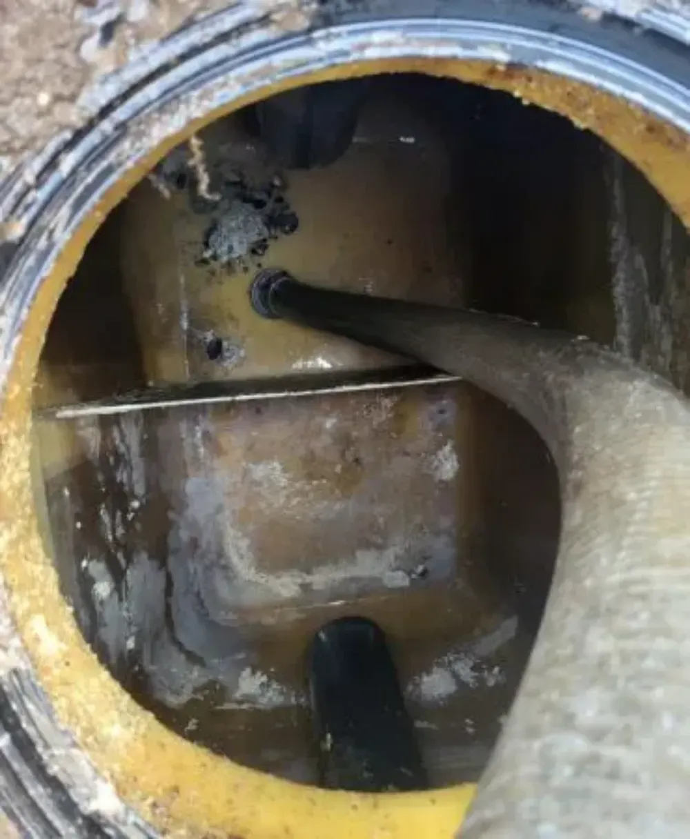 Boca de registro o abertura de depósito con el borde amarillo y una manguera en el interior; se ve agua sucia y paredes interiores oxidadas