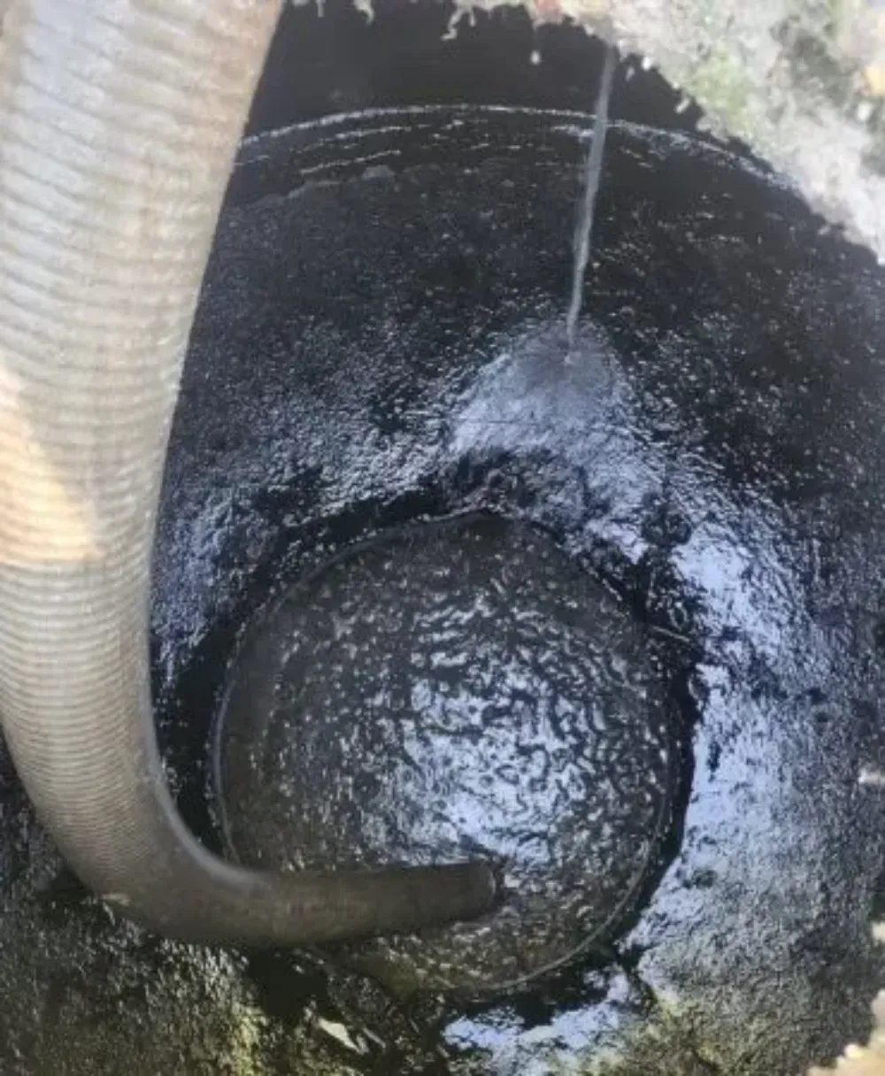 Una manguera beige dentro de un desagüe o tanque circular oscuro con residuos de lodo negro.