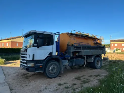 Camión cisterna blanco y naranja estacionado en un terreno de tierra bajo un cielo azul despejado