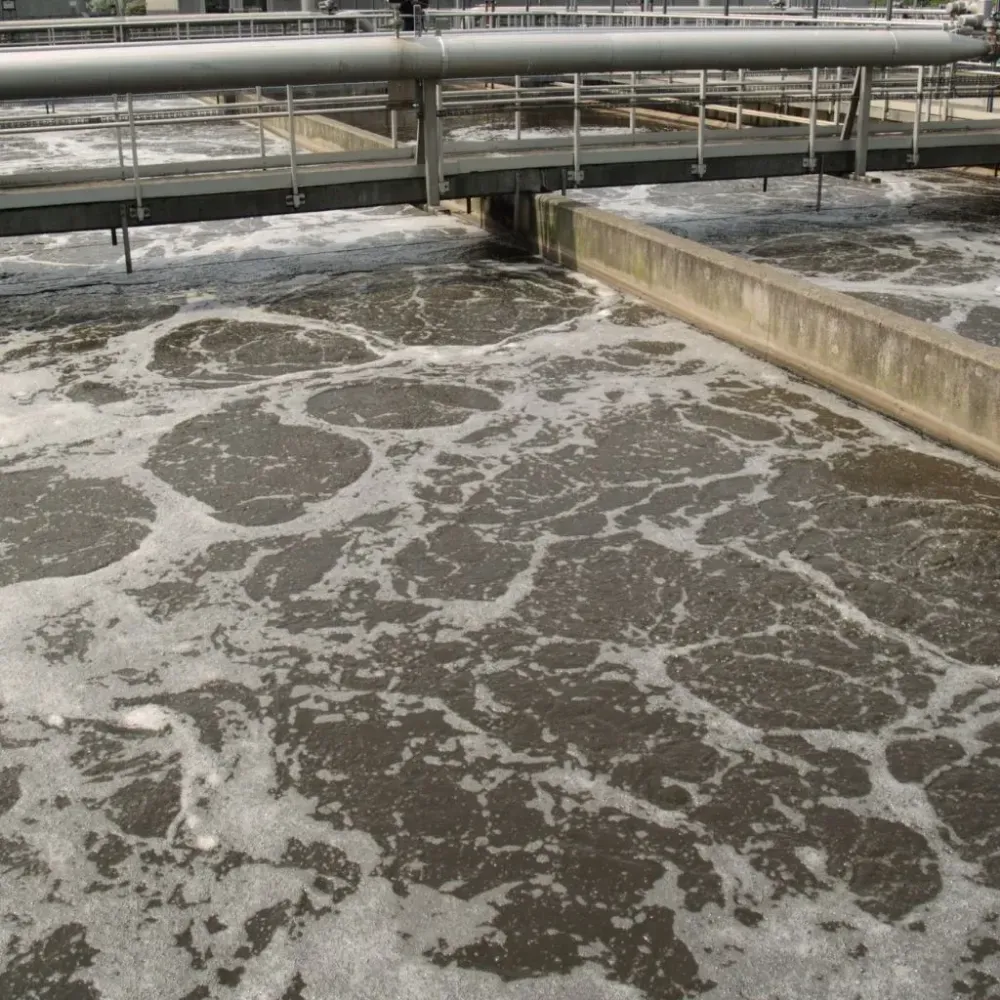 Aguas residuales espumosas que se agitan en un tanque de tratamiento bajo tuberías metálicas y un separador de hormigón