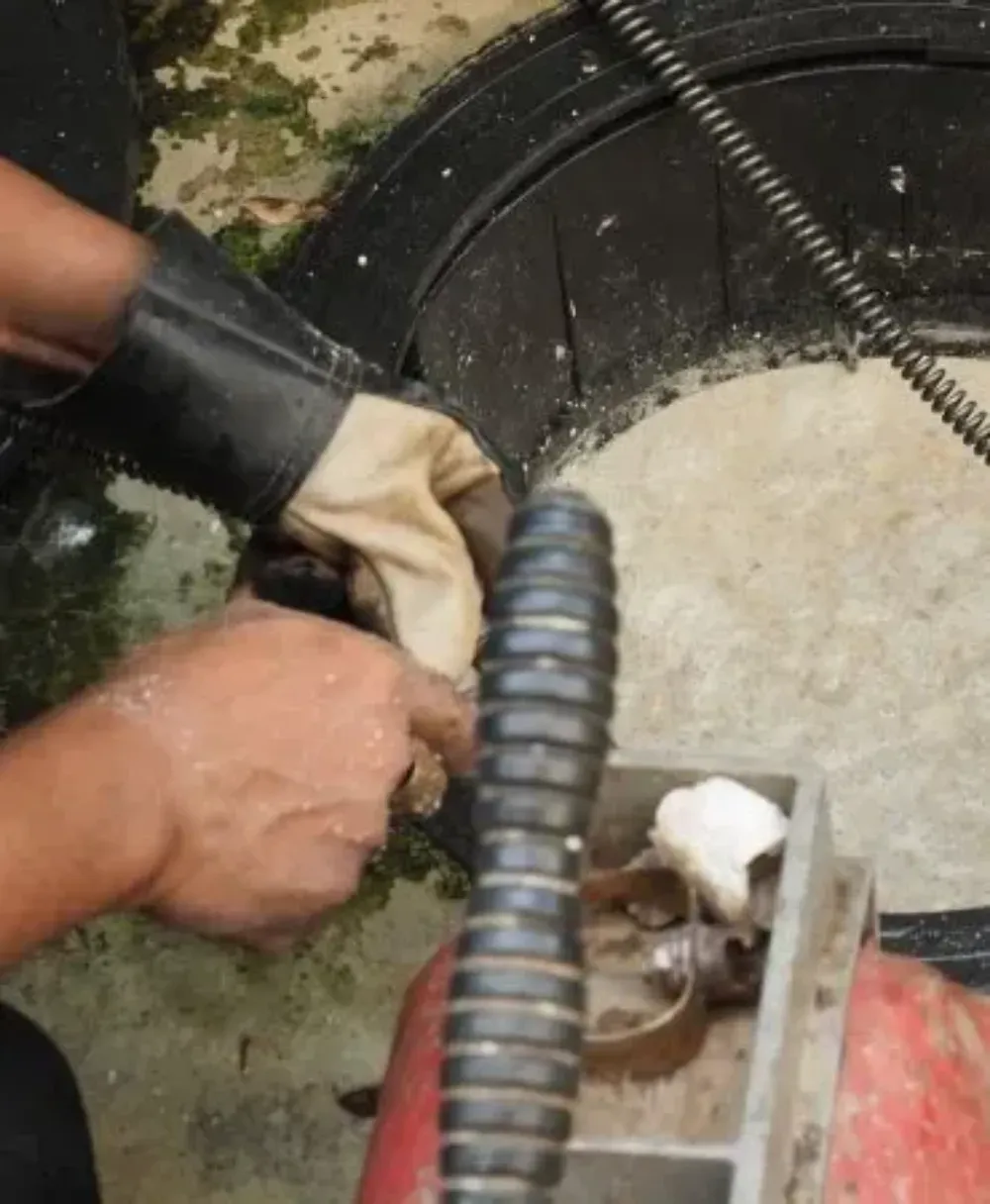 Unas manos enguantadas trabajando con una manguera negra y maquinaria metálica junto a un recipiente redondo con lodo blanco