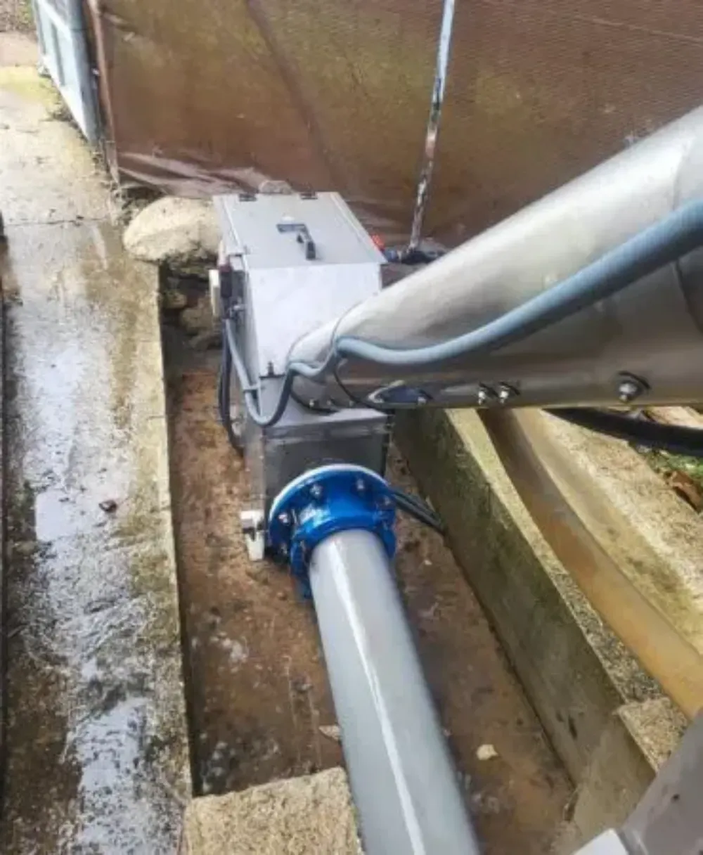 Tuberías industriales azules y grises que recorren una zanja estrecha junto a una pared marrón