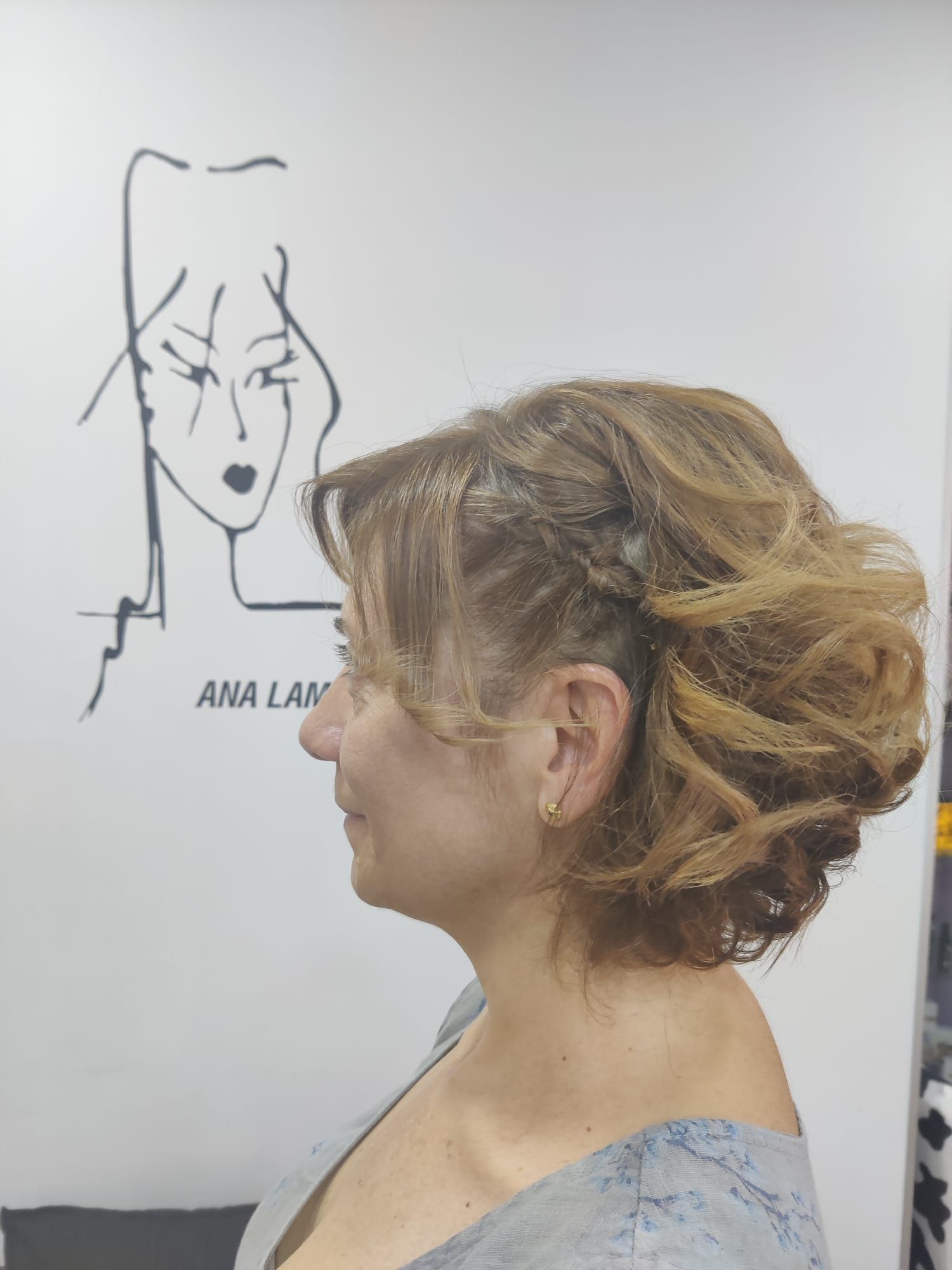 Perfil de una mujer con un elegante recogido en un salón, frente al dibujo de un rostro en la pared.