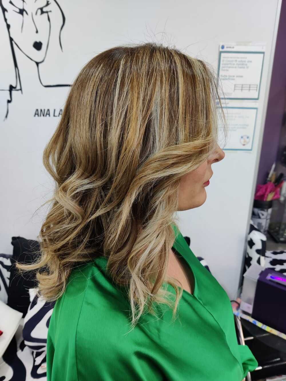 Vista lateral de una mujer con mechas rubias en capas, con una blusa verde, en una peluquería