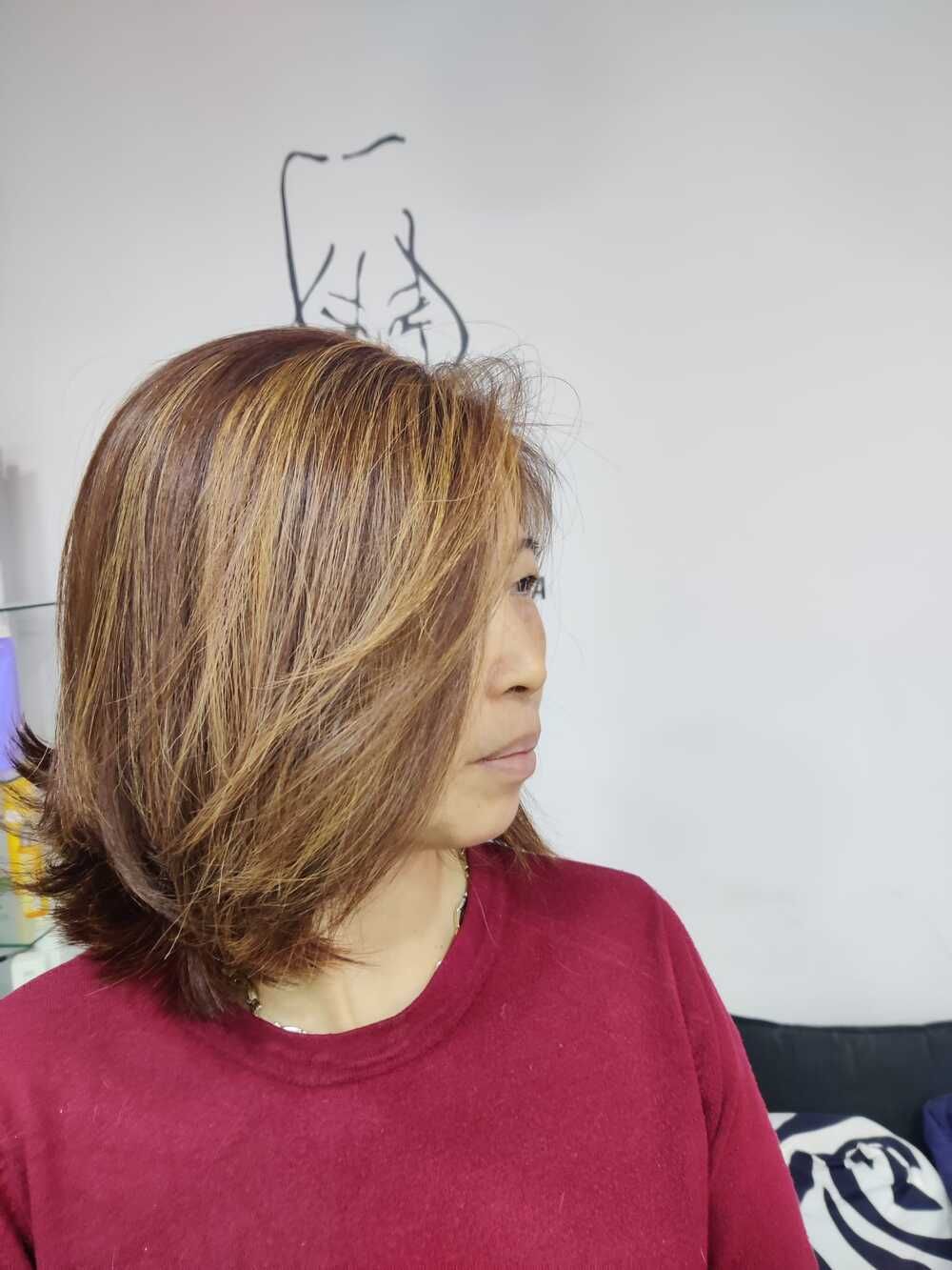 Persona con el pelo castaño hasta los hombros y un suéter rojo, de perfil frente a una pared blanca.