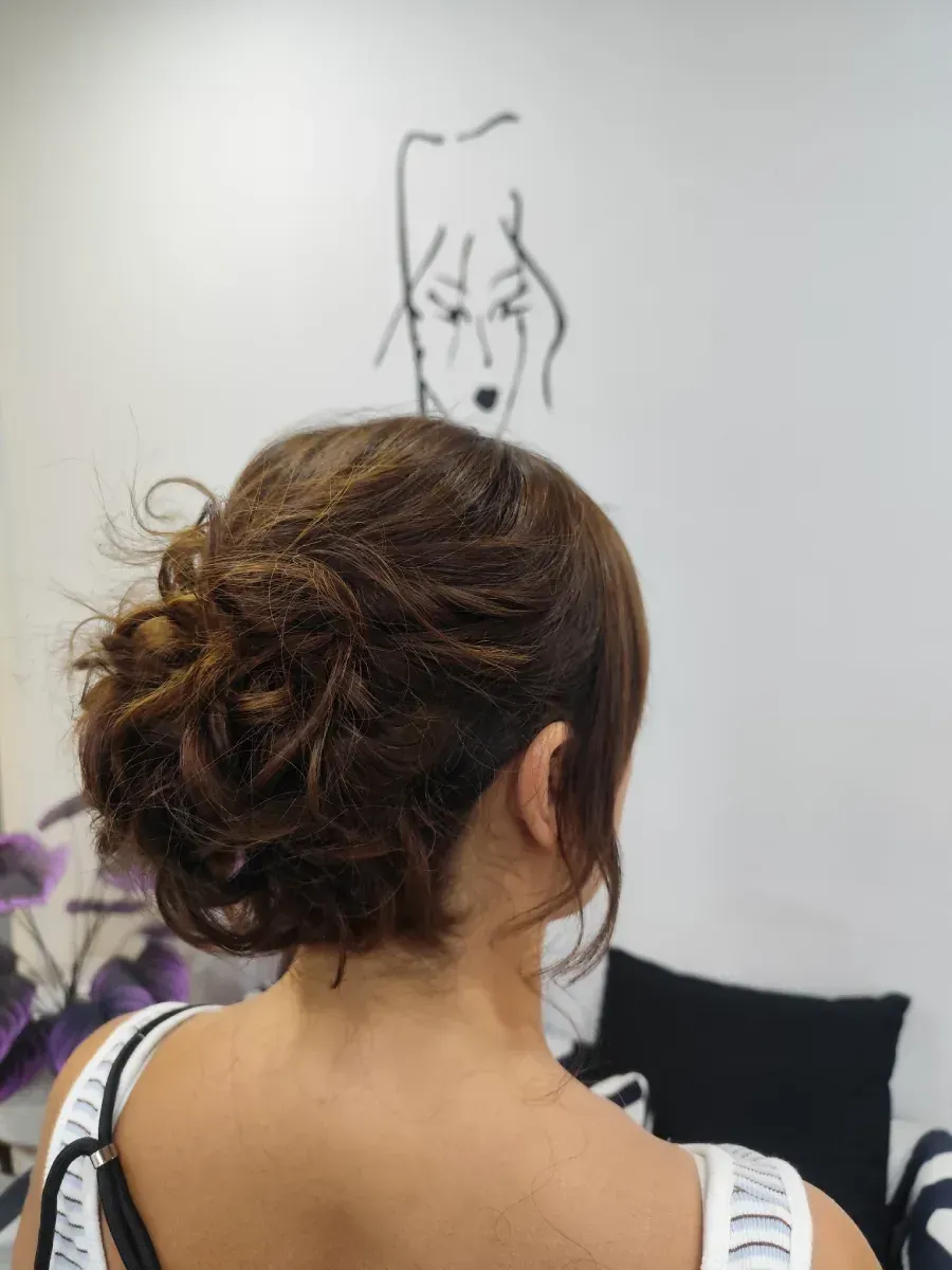 Persona con cabello oscuro recogido en un moño suelto, vista de espaldas en una habitación con un dibujo en la pared.