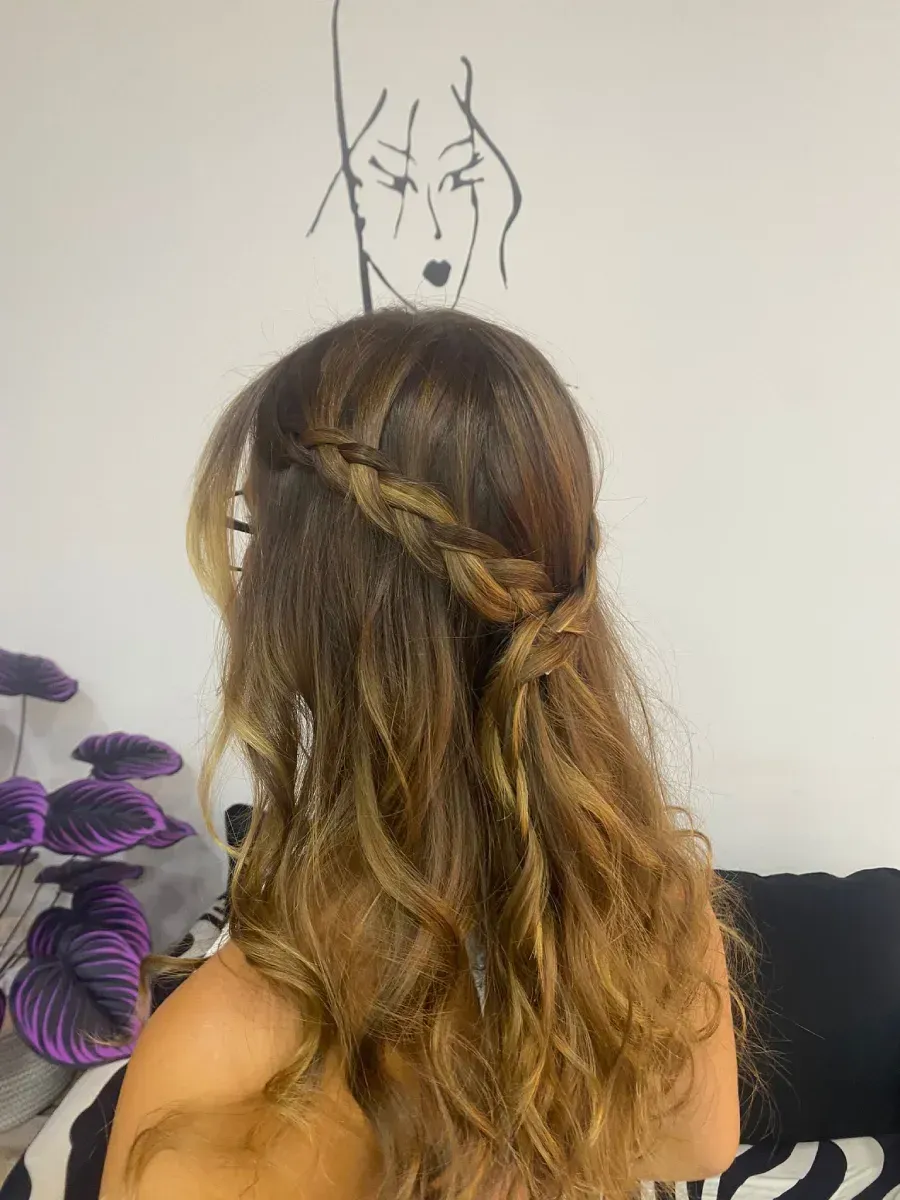 Mujer con el pelo trenzado frente a un dibujo en la pared, junto a flores moradas y un sofá negro.