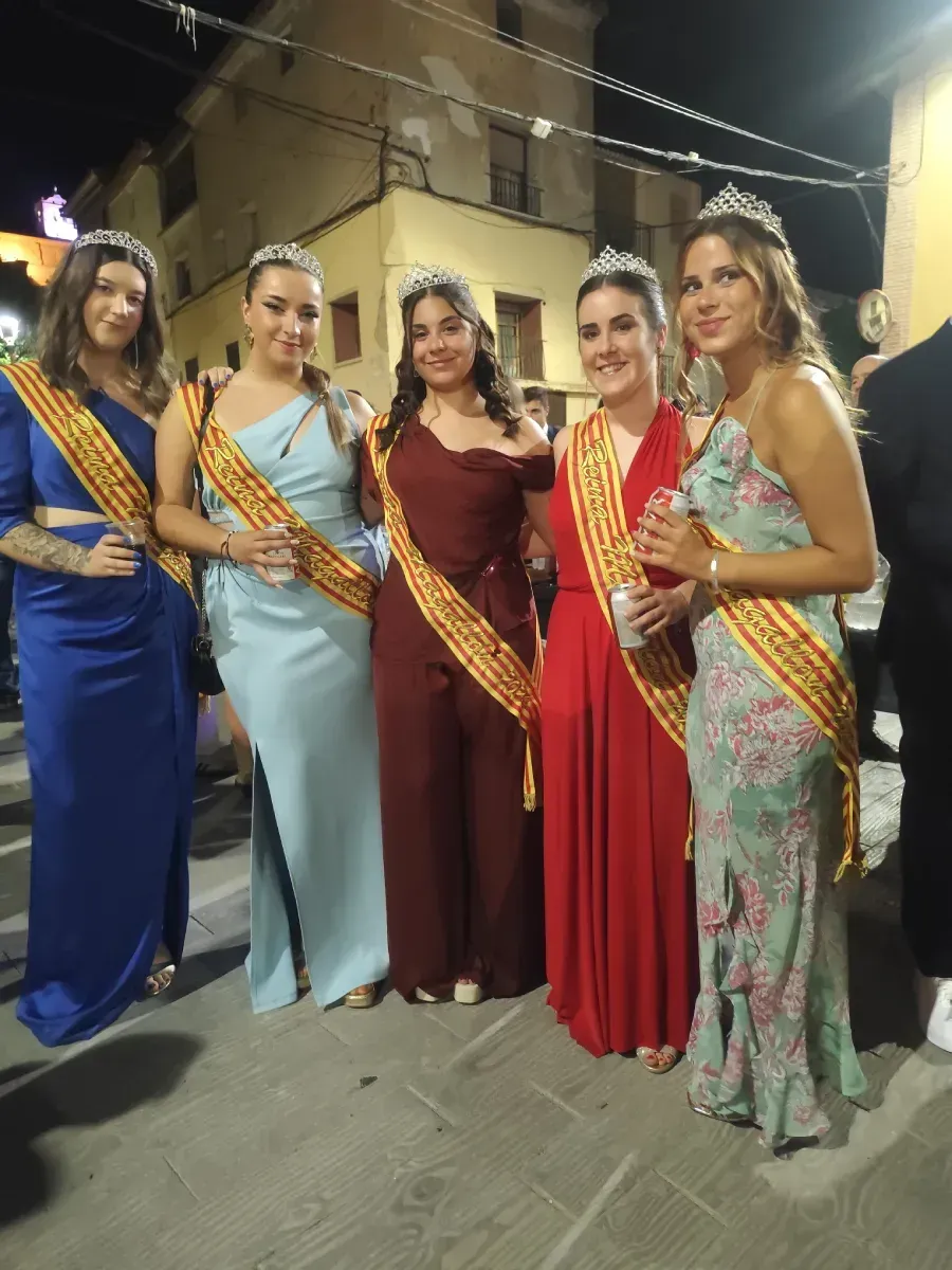 Cinco mujeres con coloridos vestidos de gala y fajas posando al aire libre por la noche en un evento.