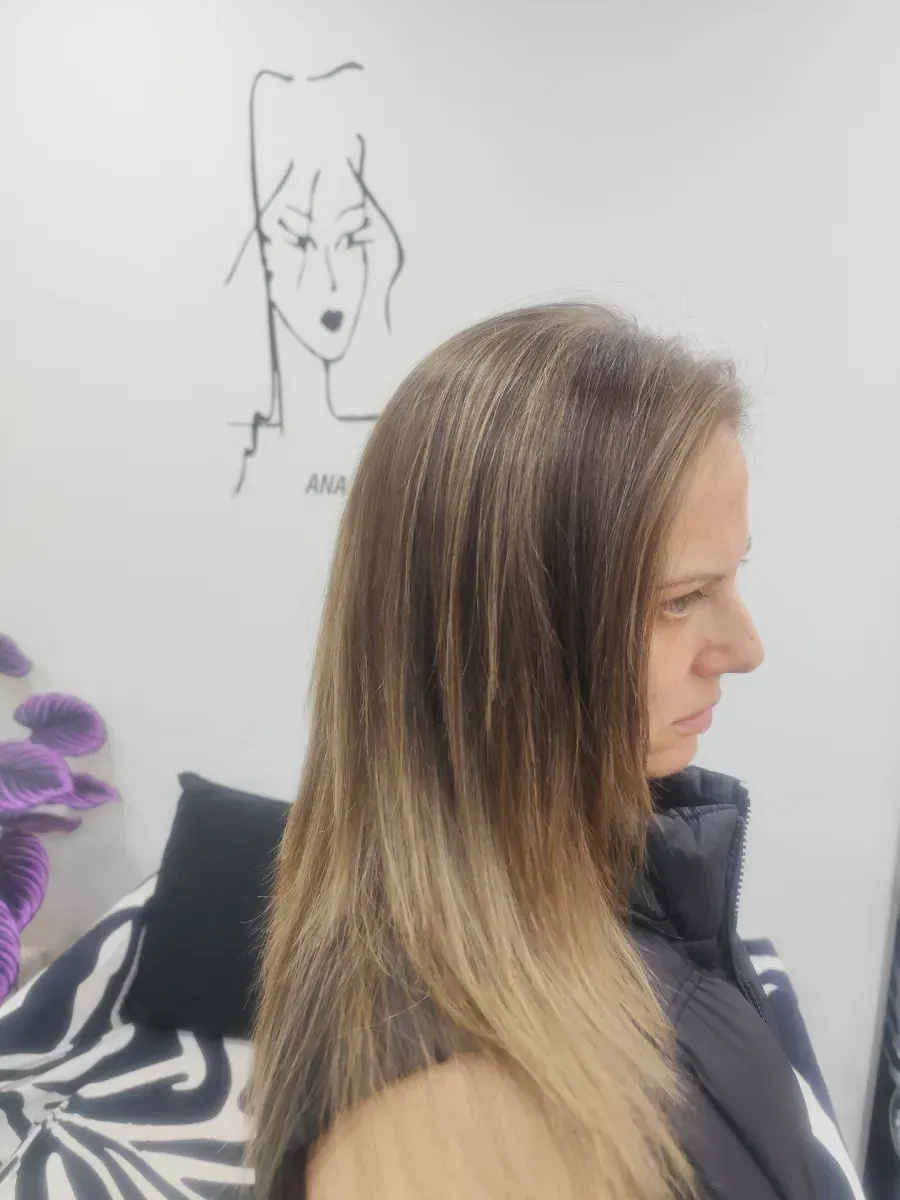Perfil de una mujer con cabello rubio liso y blusa negra, de pie en el interior de un edificio