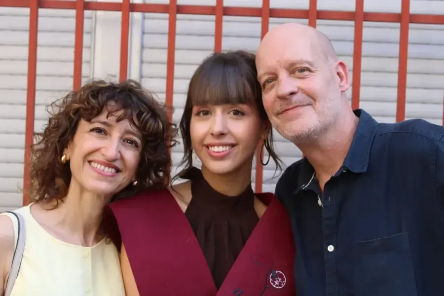 Tres personas sonriendo hombro con hombro frente a una pared de madera roja.