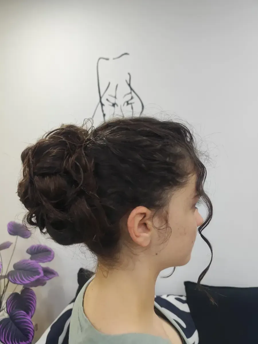 Perfil de una mujer con cabello oscuro y rizado recogido en un moño, con un dibujo de un gato en la pared detrás de ella.