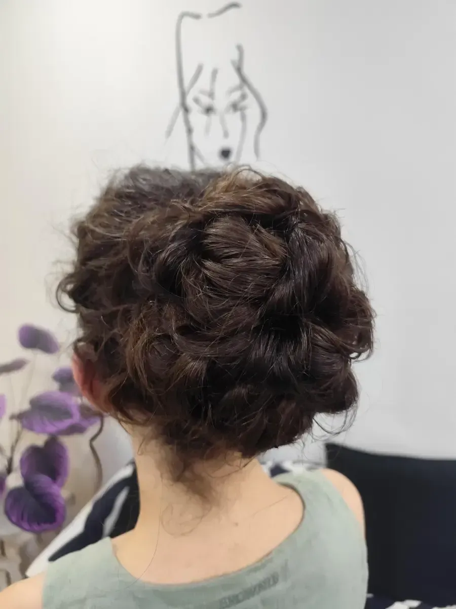 Vista trasera de una persona con cabello oscuro y rizado recogido en un moño, sentada en el interior de una casa