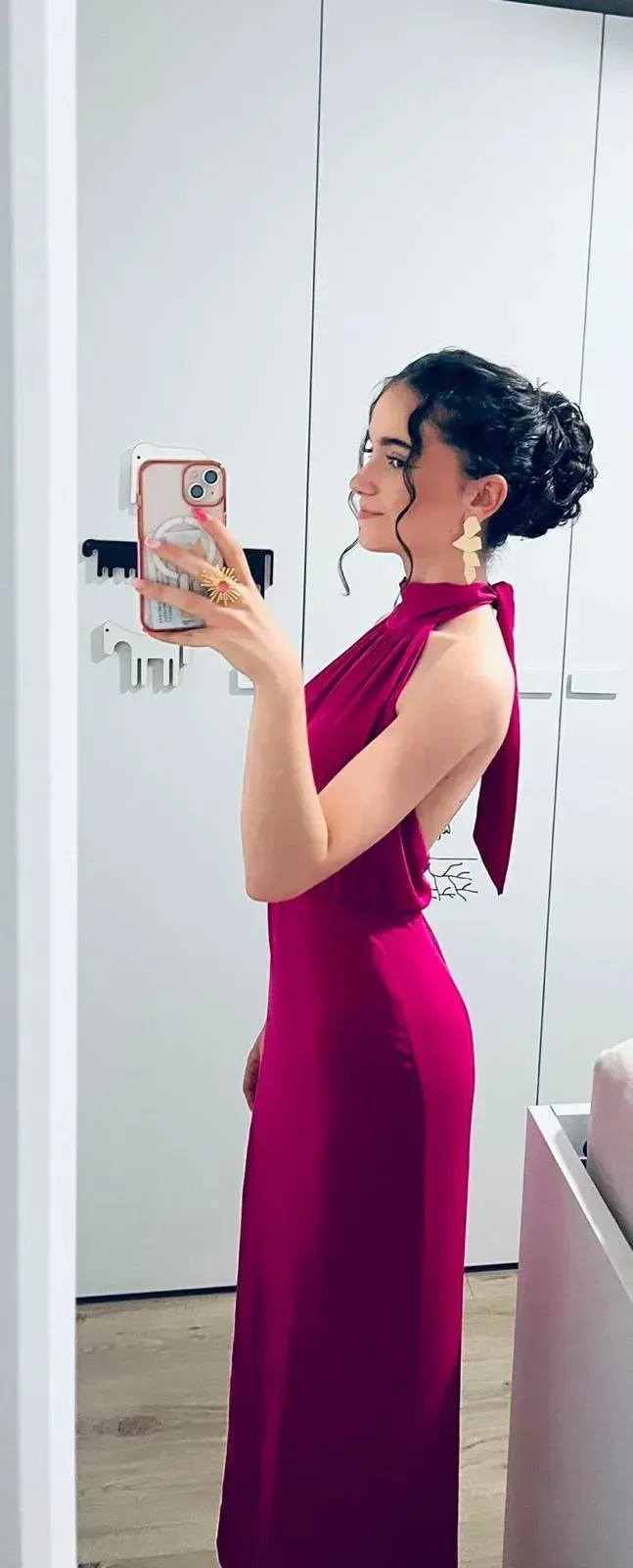 Mujer con vestido magenta tomándose una selfie frente al espejo en una habitación blanca.