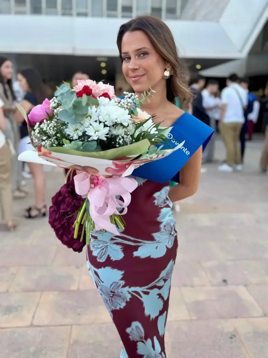 Mujer con vestido floral sosteniendo un gran ramo al aire libre en un evento formal.