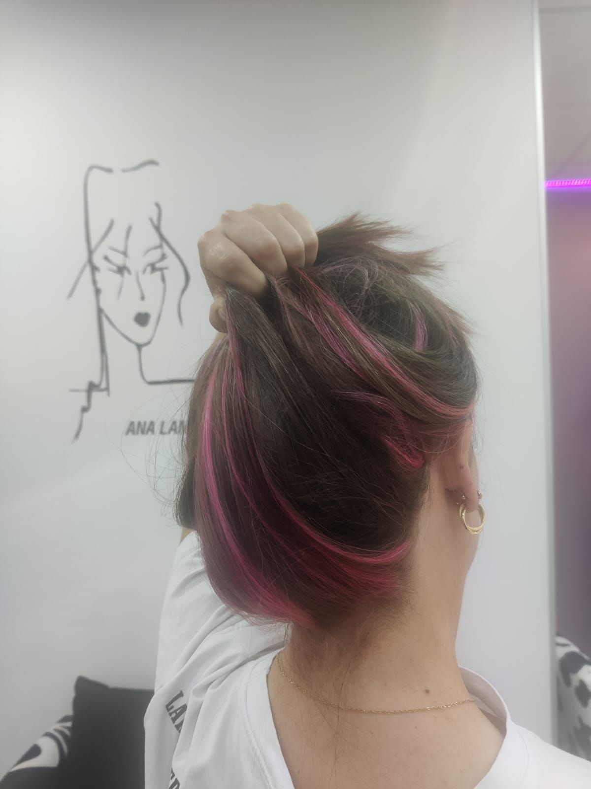 Persona arreglándose un moño con mechas rosas frente al espejo de una peluquería