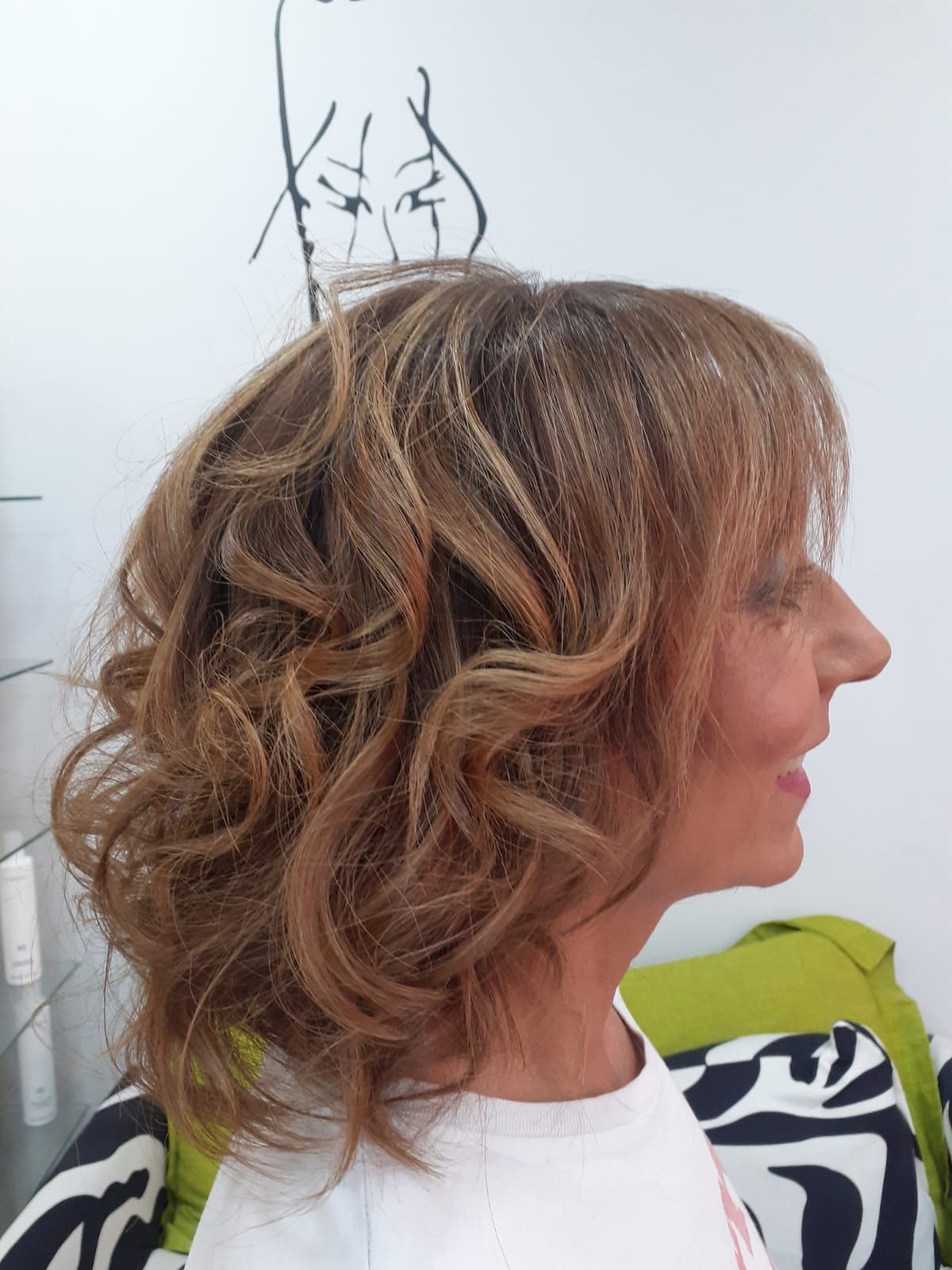 Perfil de una mujer con el pelo corto, ondulado y castaño claro, con una camisa blanca y un fondo interior liso