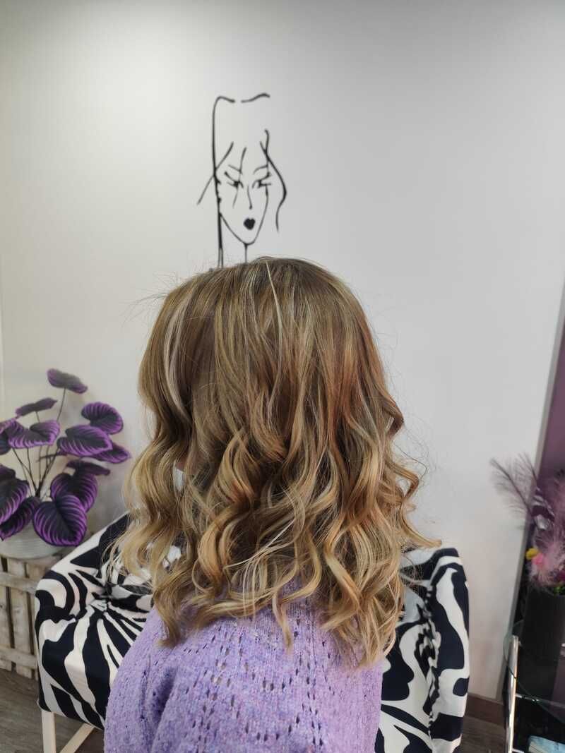 Persona de cabello castaño claro y ondulado, sentada de cara a una pared con un dibujo hecho con rotulador negro y flores moradas cerca