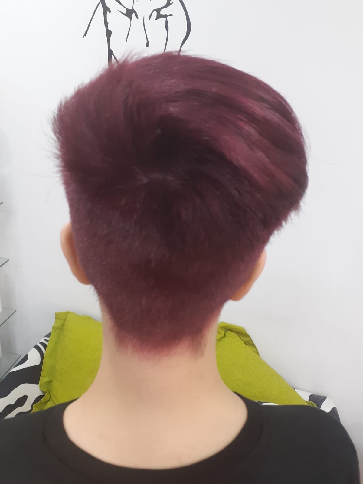 Vista trasera de una persona con el pelo corto de color burdeos y la nuca rapada, sentada en un espacio interior