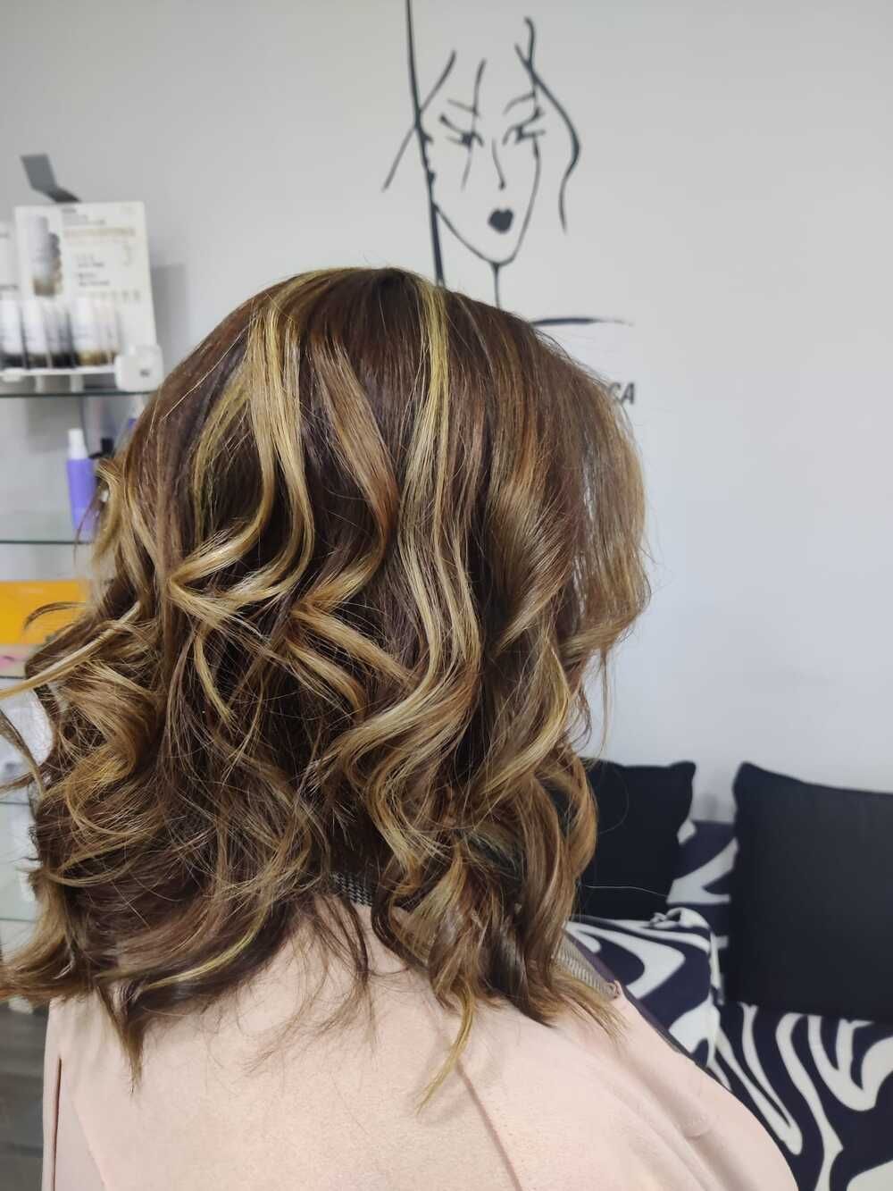 Cabello castaño ondulado con mechas rubias, visto desde atrás en un salón de belleza.