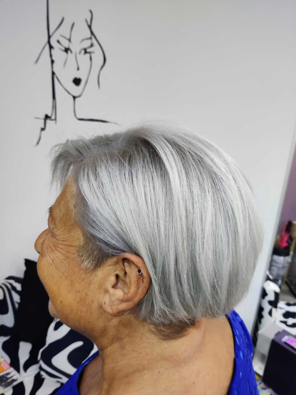 Vista de perfil de una mujer de pelo corto y plateado bajo un dibujo de líneas negras en una pared
