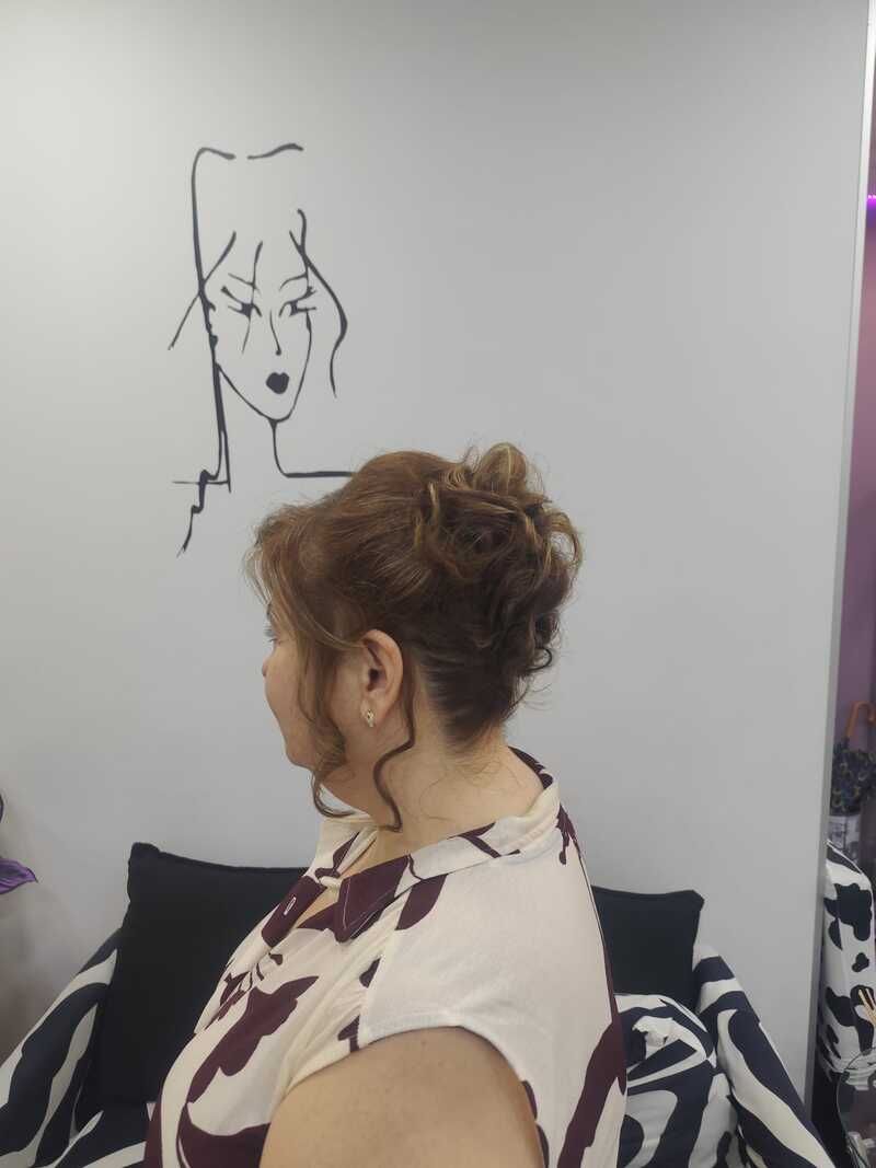Mujer de perfil mirando un dibujo en la pared encima de una cama, con una cortina morada y ropa de cama estampada.