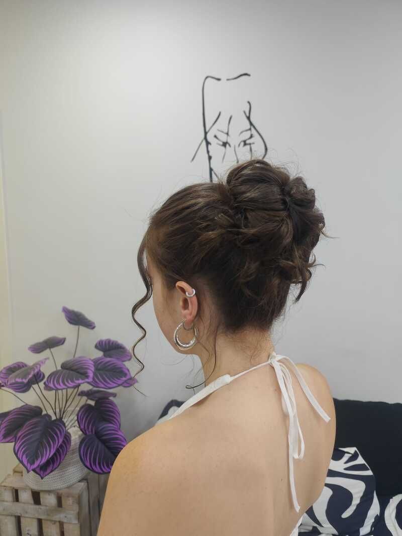 Mujer con un elegante moño, vista de perfil junto a unas flores moradas y un dibujo en una pared.