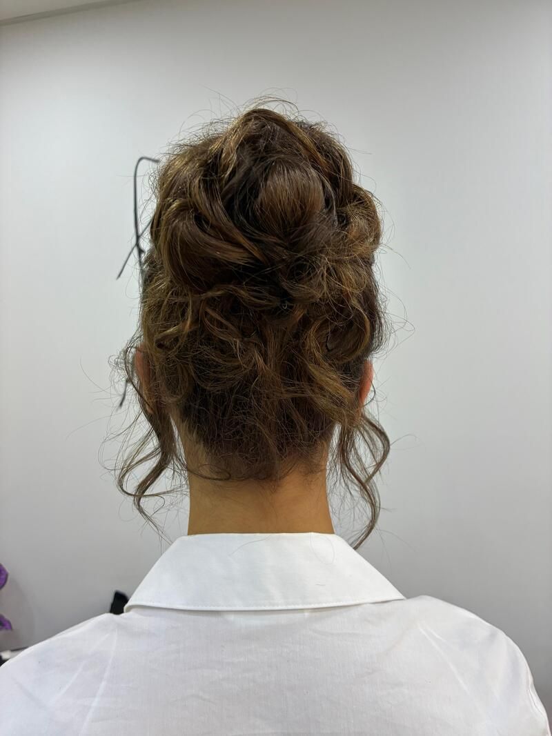 Persona vista de espaldas, con el pelo recogido en un moño despeinado y una camisa blanca con cuello.