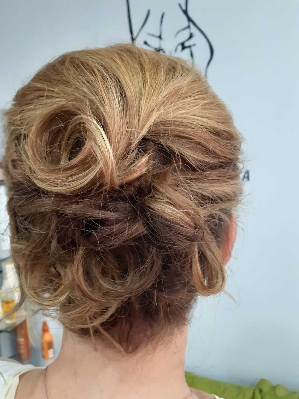 Vista trasera de un peinado recogido con mechas rubias y rizos sueltos, sujeto a la altura de la nuca