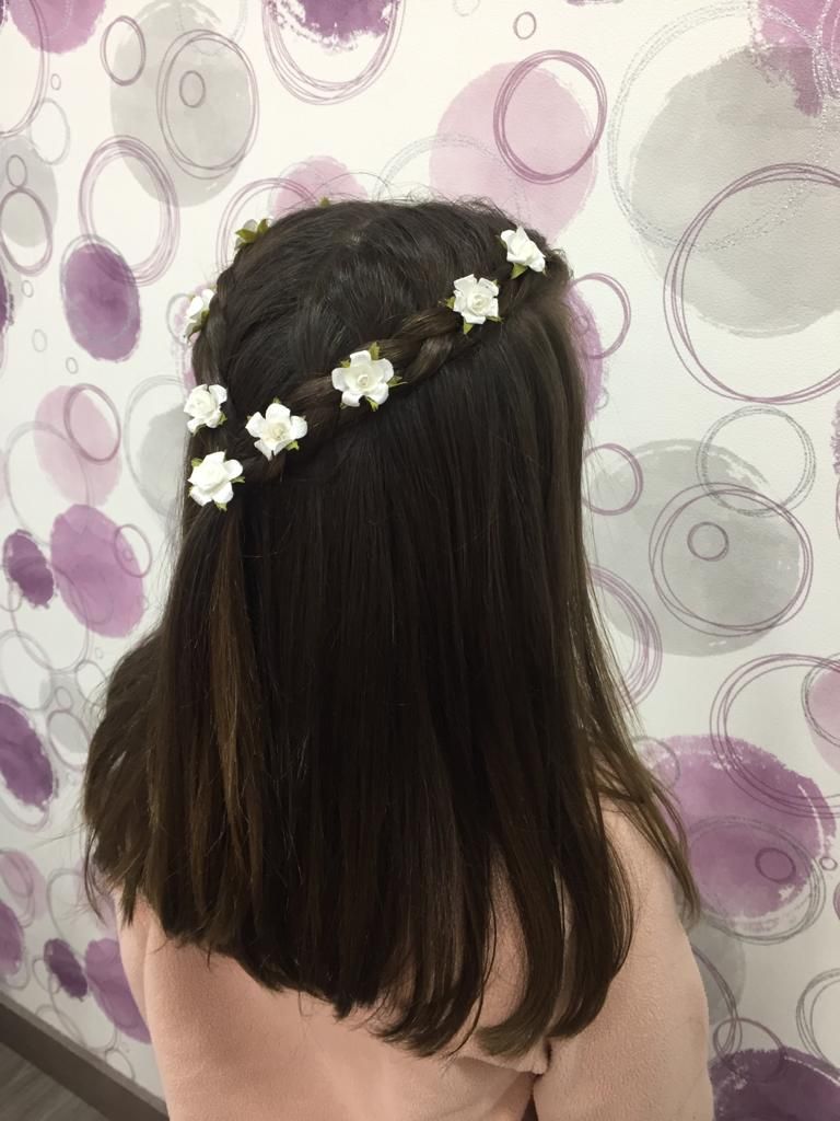 Vista trasera de una persona con el pelo largo y oscuro y una diadema de flores blancas, frente a una pared estampada