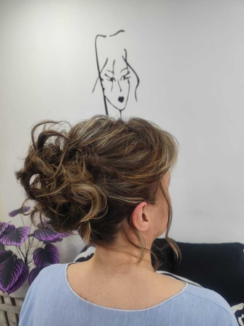 Mujer de cabello castaño recogido en un moño suelto, vista desde atrás, en una habitación con un dibujo sencillo en la pared.