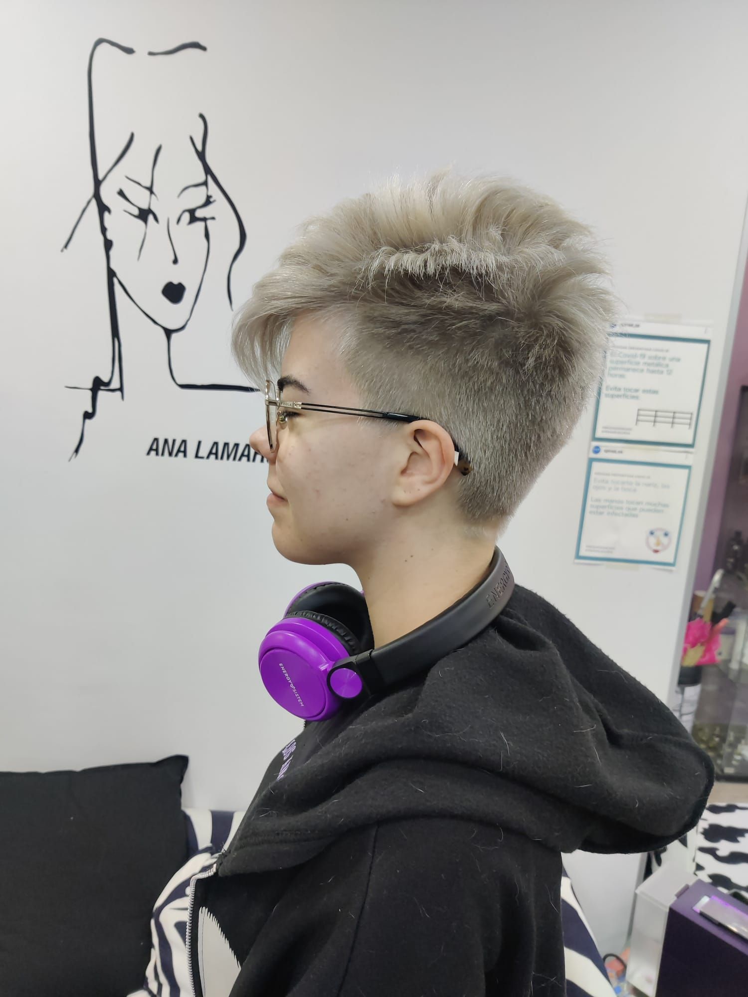 Persona de perfil con el pelo corto y canoso, con auriculares morados, junto a un dibujo artístico en la pared.