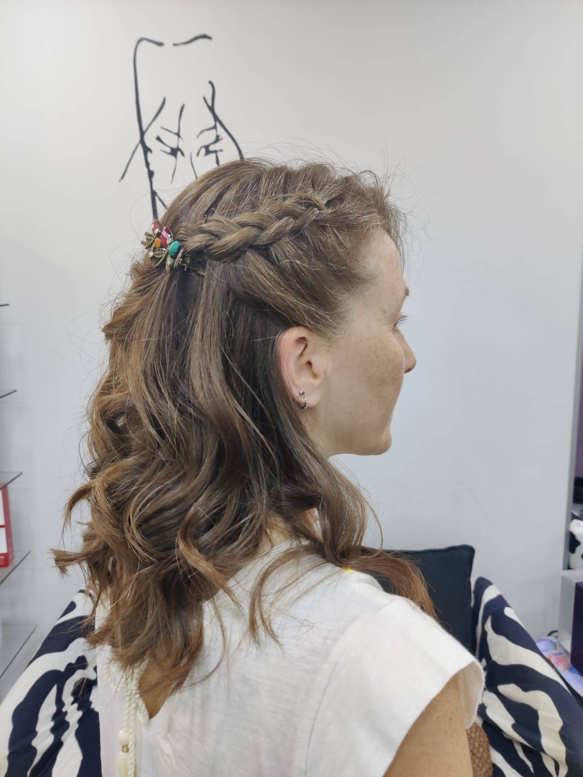 Vista de perfil de una mujer con el pelo castaño trenzado, vestida con una camiseta blanca y sentada junto a una pared lisa.