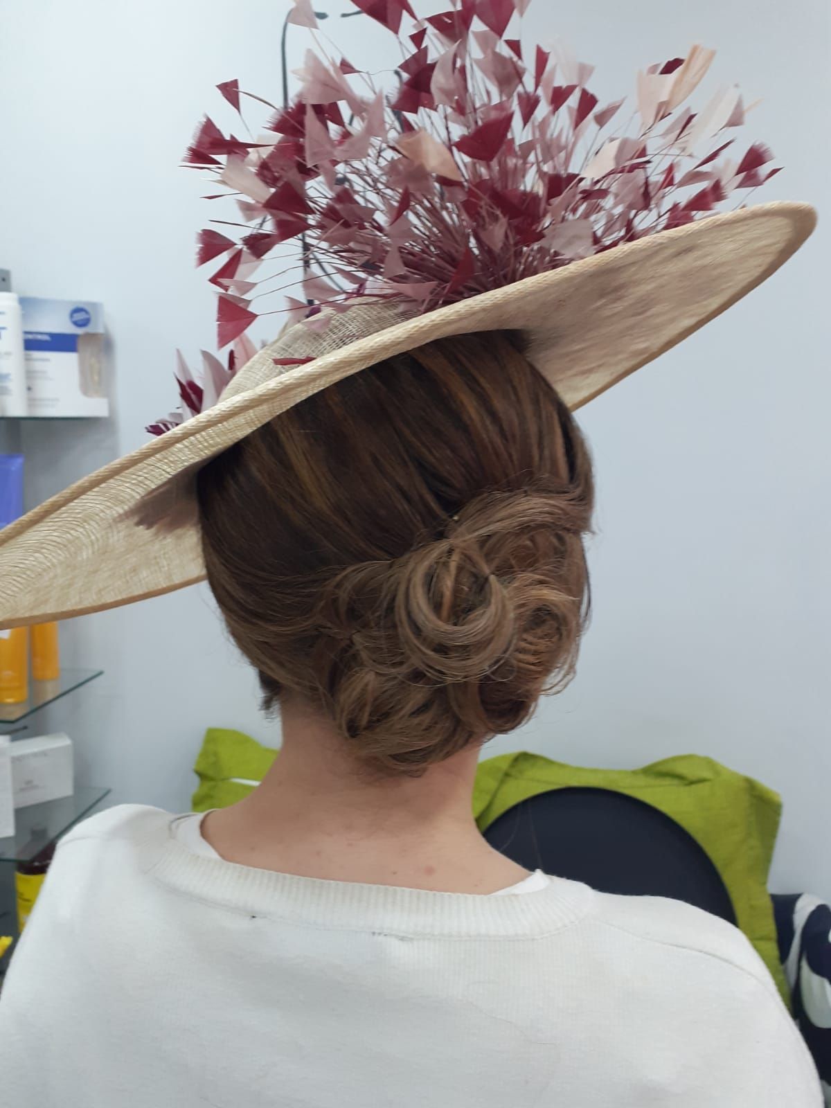 Mujer vista de espaldas con un sombrero beige grande, adornado con flores rosas, y un elegante moño bajo