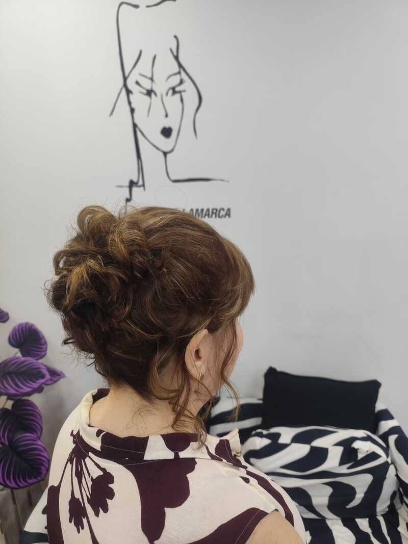 Vista trasera de una persona con el pelo recogido en un salón, de cara a un boceto de cabello en la pared sobre un fondo blanco.