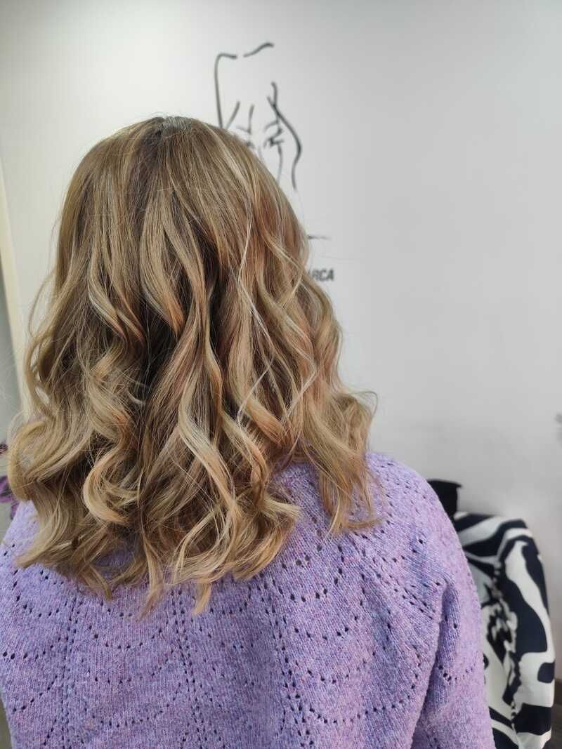 Vista trasera de una persona con el pelo rubio ondulado y un suéter color lavanda en interiores